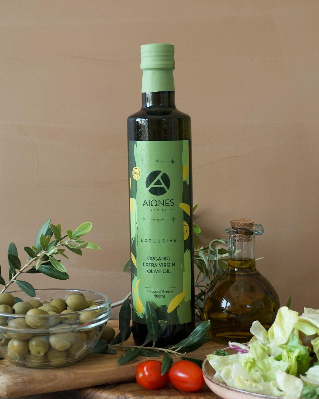 Bottle of AEONS organic extra virgin olive oil with olives and tomatoes on a wooden board.